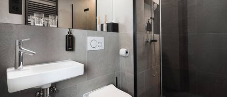 A modern bathroom with a white sink, a toilet, and a glass-enclosed shower.