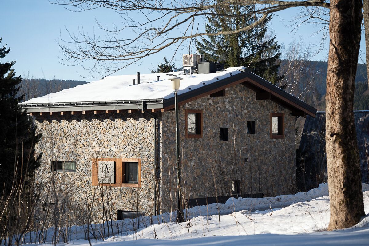 A stone building with a sloped roof, surrounded by snow and trees.