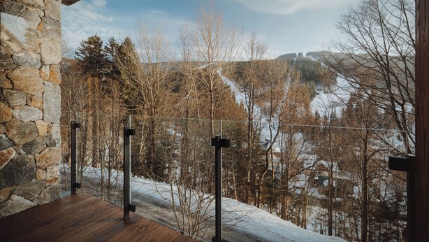 A stone wall, wooden deck, metal railing, and a view of a snowy landscape with trees. - Avenue Chalet (Špindlerův Mlýn)