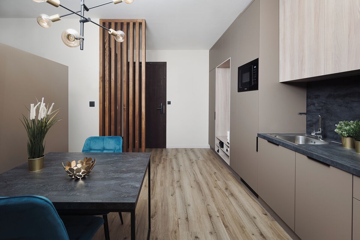 A modern kitchen with a dark countertop, wooden flooring, and a built-in microwave.