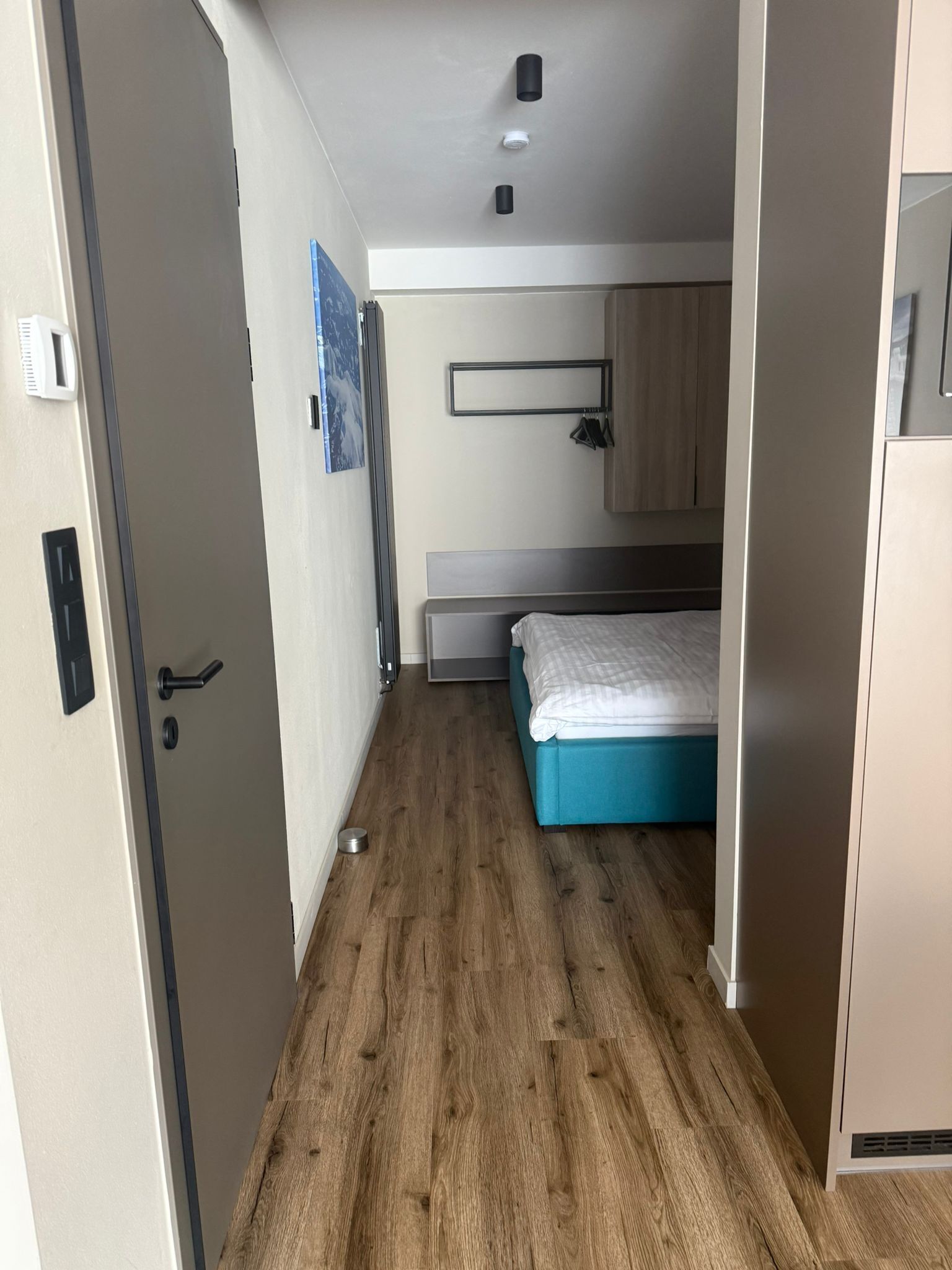 A compact room with a bed, a small kitchenette, and a door leading to another area.