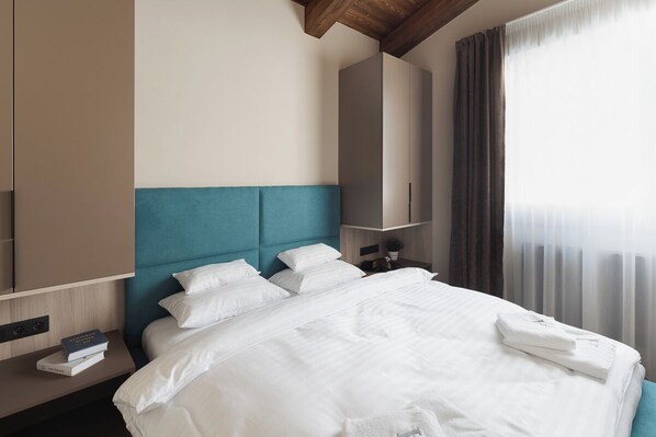 A hotel room with a bed, a nightstand, a wardrobe, and a window with curtains. - Avenue Chalet (Špindlerův Mlýn)