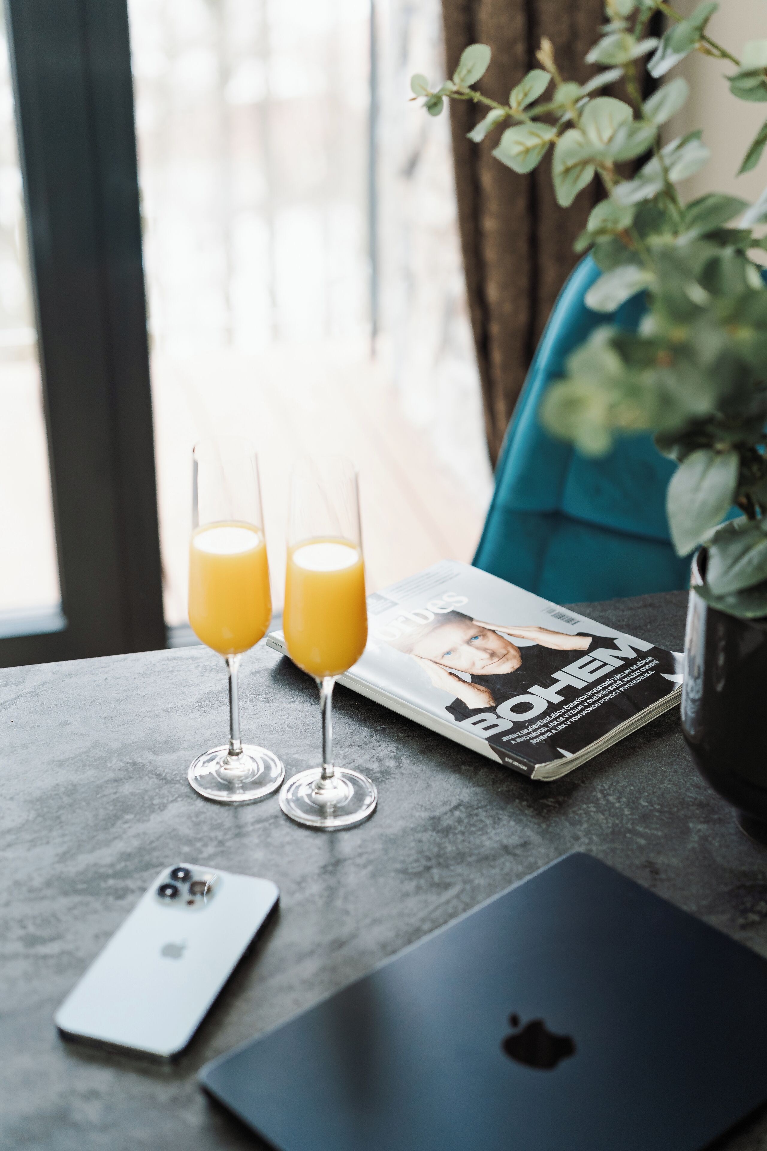 Una mesa con dos vasos de jugo de naranja, una revista, un teléfono inteligente y una computadora portátil.