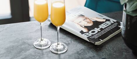 Una mesa con dos vasos de jugo de naranja, una revista, un teléfono inteligente y una computadora portátil.