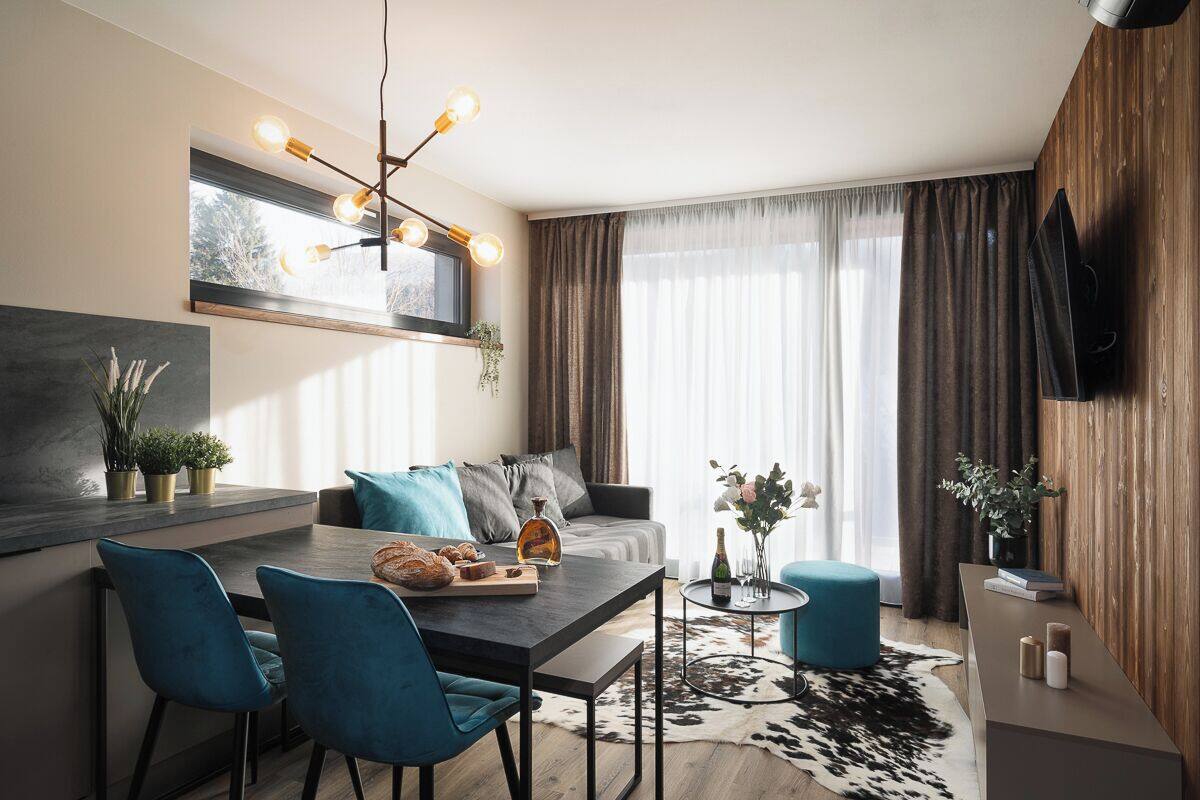 A modern living room with a dining area, a mounted TV, and a large window with curtains.