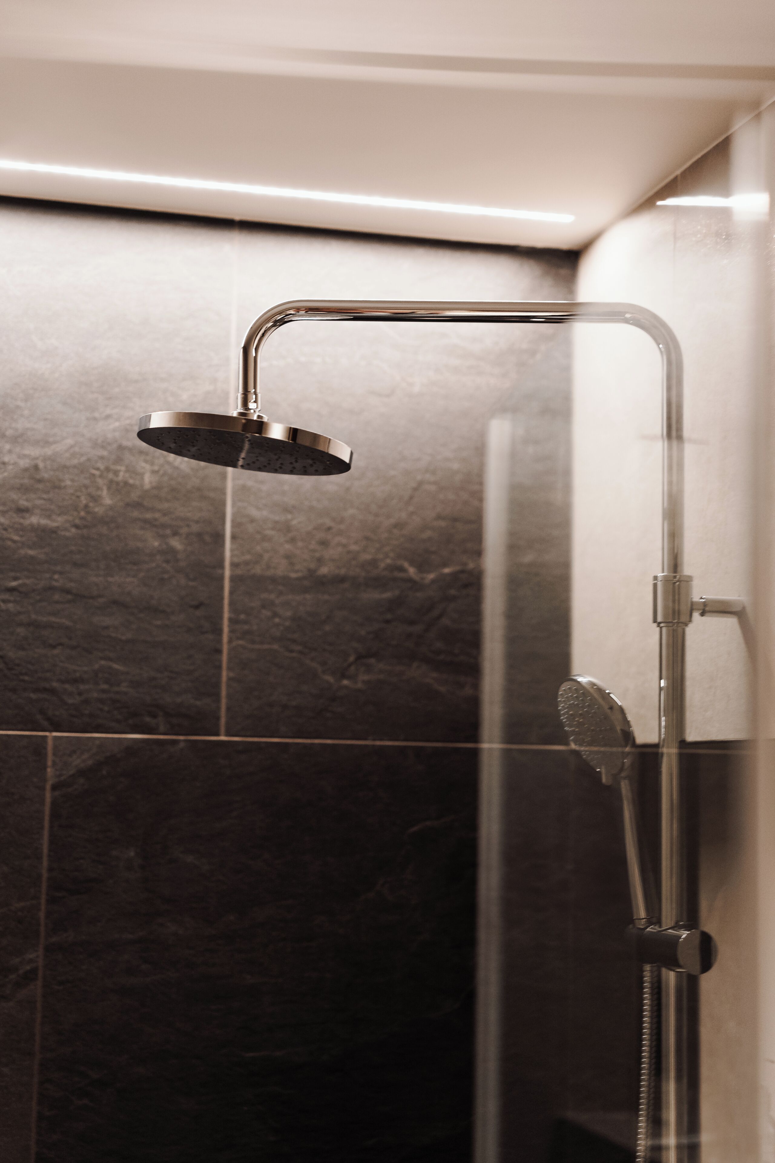 A shower with a handheld showerhead and a wall-mounted control.