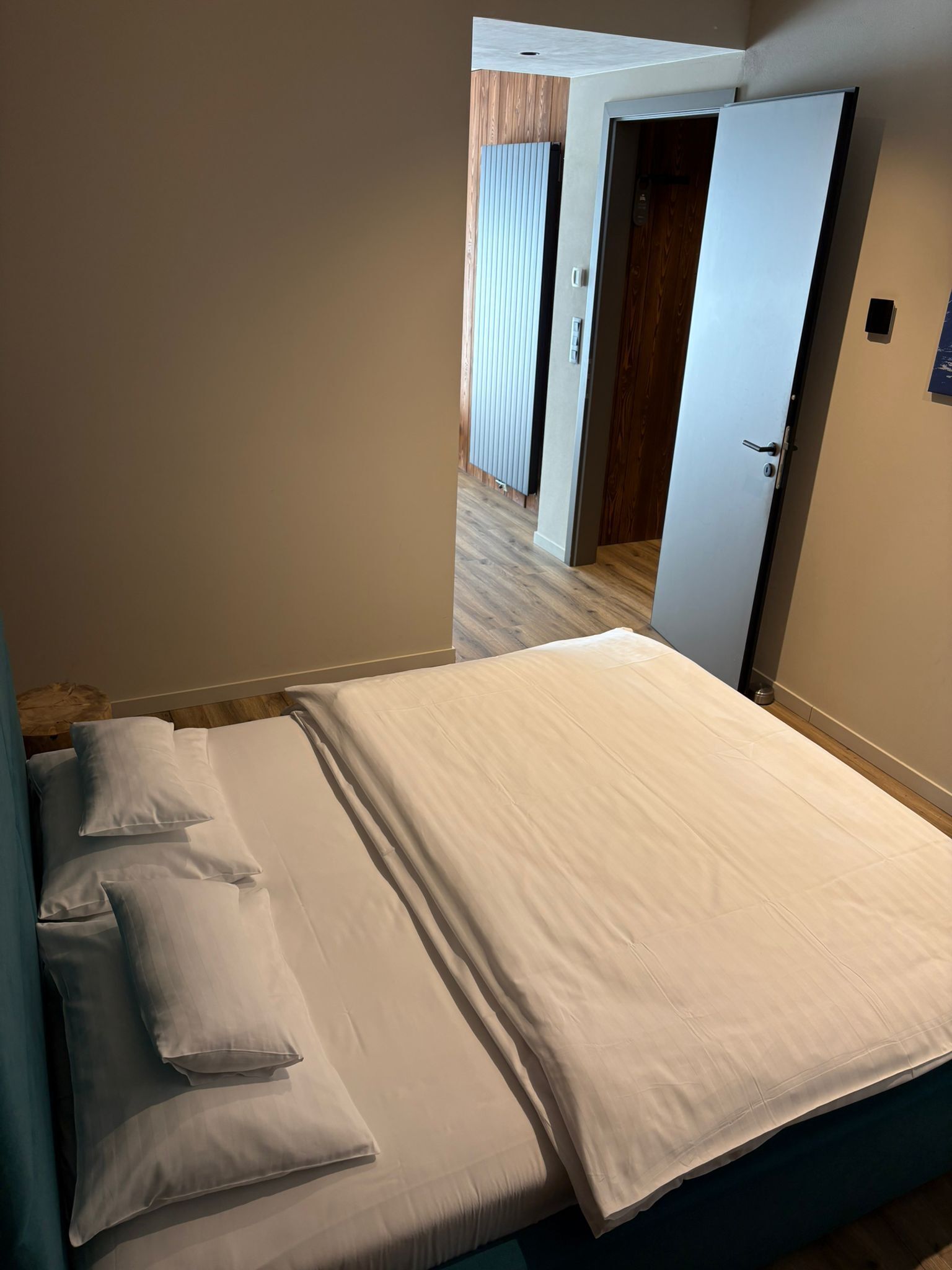 A bedroom with a bed, pillows, a door, and a view of another room.