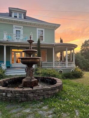 A house with a fountain in the front yard, a porch with chairs, and a sunset in the background. - Elegant Historic Villa with hot tub! (Saint-Malo)