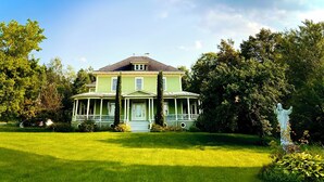 A large, two-story house with a wrap-around porch, surrounded by lush greenery and trees.