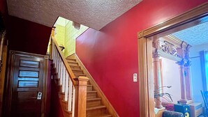 A wooden staircase leading to a room with a red wall and a ceiling with a circular light fixture.