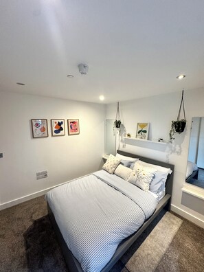 A bedroom with a bed, a bedside shelf, and wall-mounted artwork.
