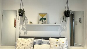 A bedroom with a bed, pillows, a bedside table, a mirror, and hanging plants. - Modern Canal Side 1BR | Balcony | Near Wembley & Tube (Wembley)
