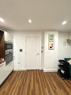 A modern kitchen with built-in appliances, a wooden floor, and a white door.