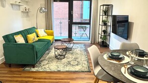 A modern living room with a green sofa, a dining table set for four, and a balcony with a view of a brick building. - Modern Canal Side 1BR | Balcony | Near Wembley & Tube (Wembley)