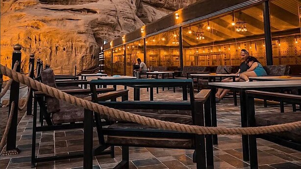 An outdoor dining area with tables and benches, surrounded by a rope barrier, set against a backdrop of rock formations. - Victoria Luxury Camp (Wadi Rum)