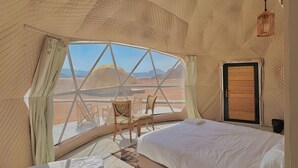 A cozy, dome-shaped room with a bed, a small table, and chairs, offering a view of a desert landscape. - Victoria Luxury Camp (Wadi Rum)