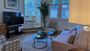 Un salon comprenant un téléviseur, un canapé, un fauteuil et une table sur laquelle est posé un jeu d’échecs.