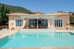 A house with a swimming pool, a covered patio with furniture, and a mountainous backdrop. - Villa Olivia – Panoramic Sea View Retreat (Lefkada)