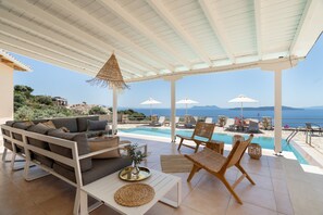 Un espacio de estar al aire libre techado con piscina, sillones y un sofá.