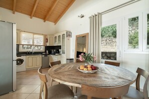 A kitchen with a round wooden table, a washing machine, and a sink. - Villa Olivia – Panoramic Sea View Retreat (Lefkada)