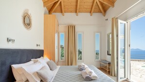 Un dormitorio con cama, almohadas, mesita de noche, espejo y vistas al exterior.