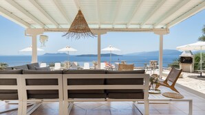 Un espacio de estar al aire libre con techo, que ofrece vistas al mar y a las montañas.