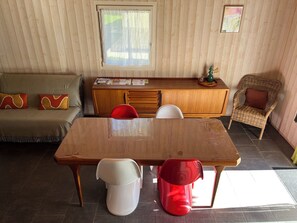Ein gemütliches Wohnzimmer mit einem Holztisch, einer Couch, einem roten Sessel und einem Korbstuhl.