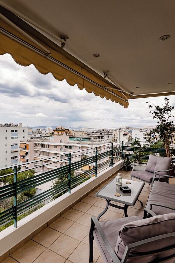 A balcony with a view of a cityscape, furnished with a table and chairs, and a potted plant.