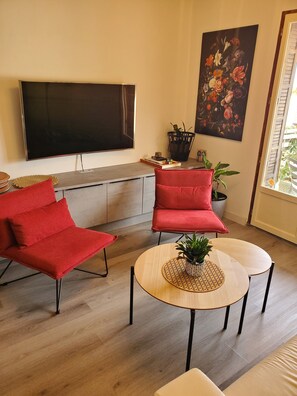 Ein modernes Wohnzimmer mit Fernseher, roten Sesseln, einem Couchtisch und einer Topfpflanze.
