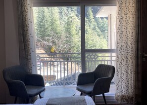 Une pièce avec deux chaises et une table, une grande fenêtre donnant sur des arbres et un balcon.