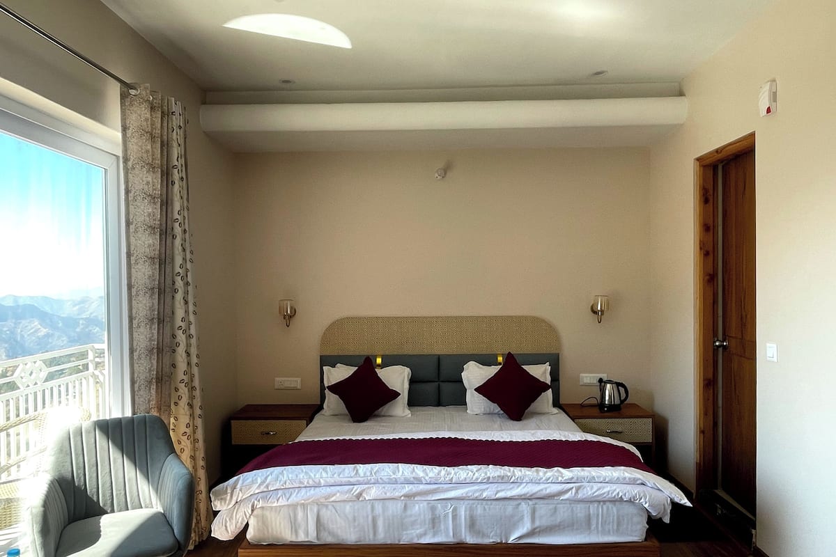 Un dormitorio con una cama grande, una silla, una mesita de noche y vistas a las montañas.