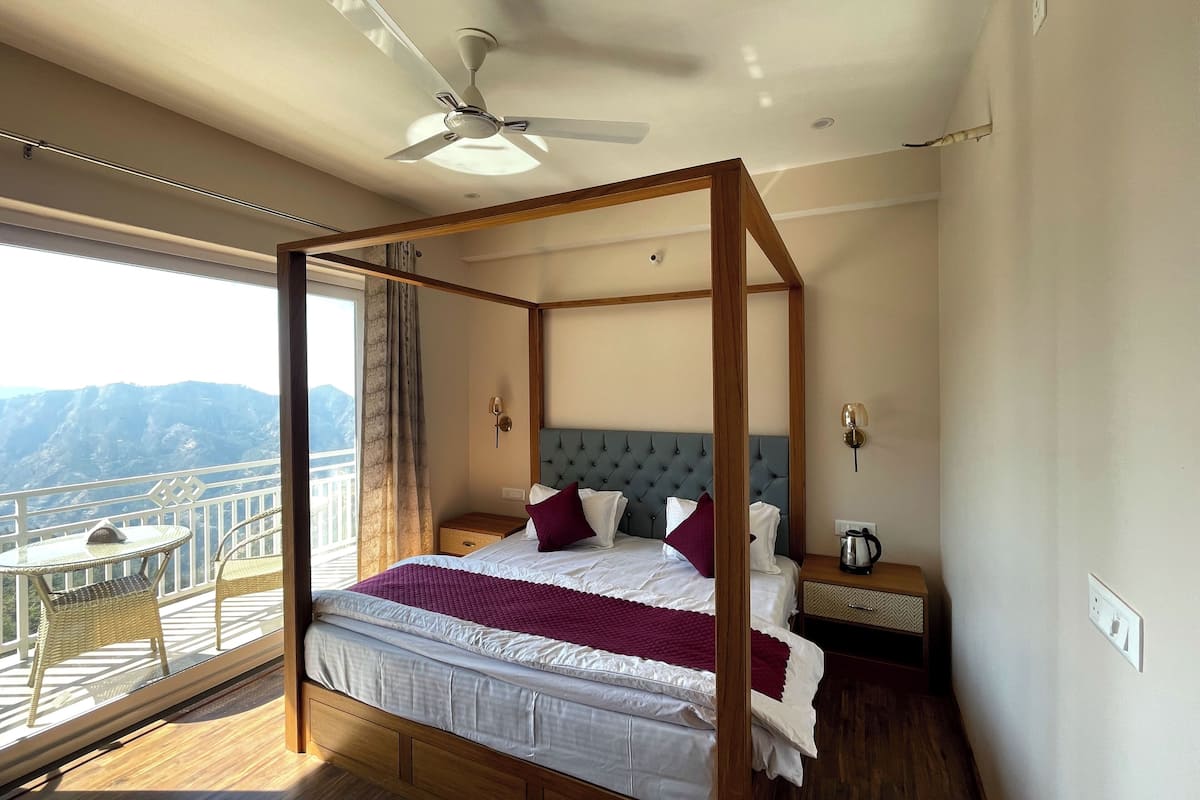 Una cama con dosel con vistas a montañas, un balcón con sillas de mimbre y un ventilador de techo.