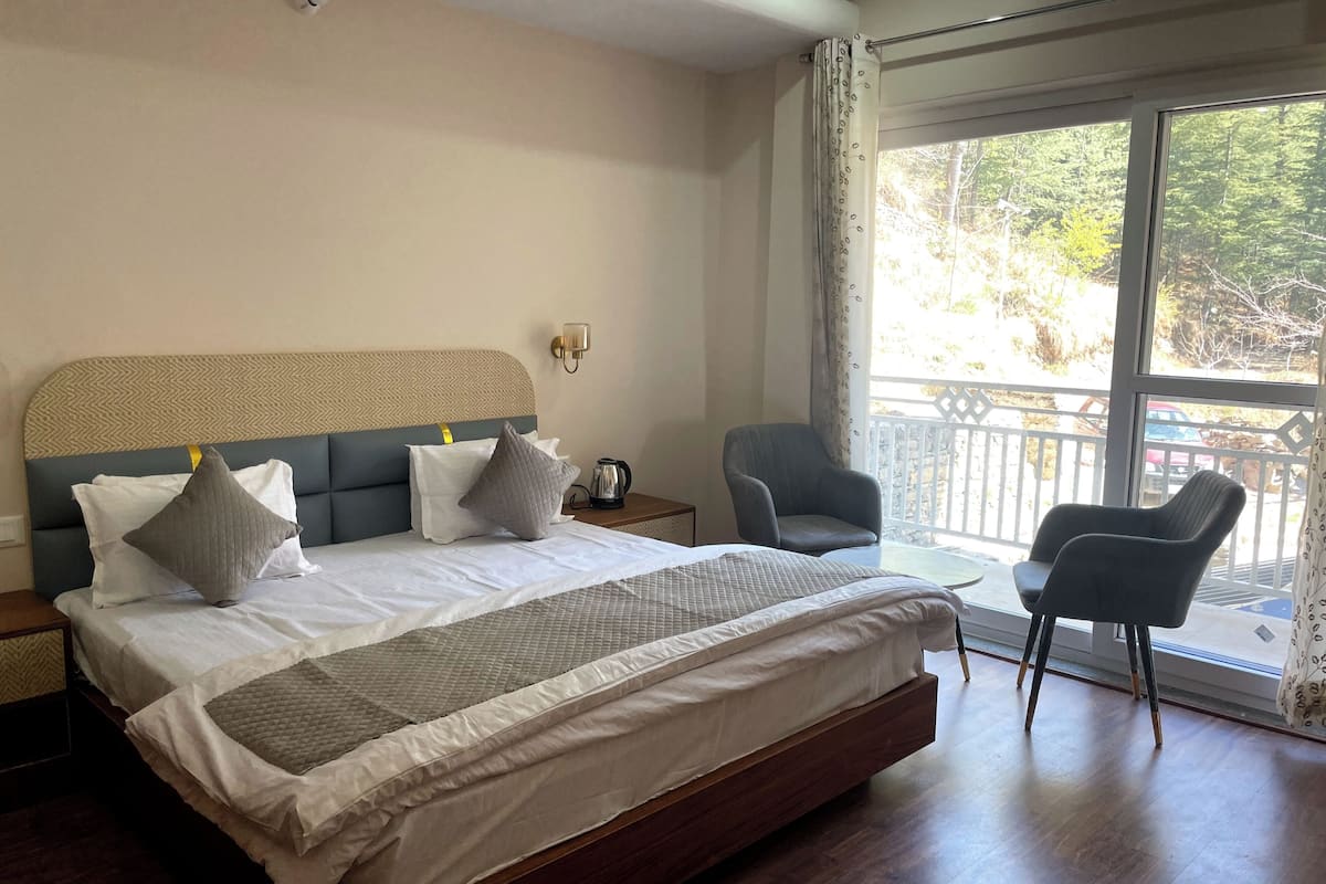 Un dormitorio con una cama grande, dos sillas, una mesita de noche y una ventana con vista a árboles.