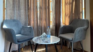 Een kamer met twee grijze fauteuils en een kleine ronde tafel met een fles water en een glas.