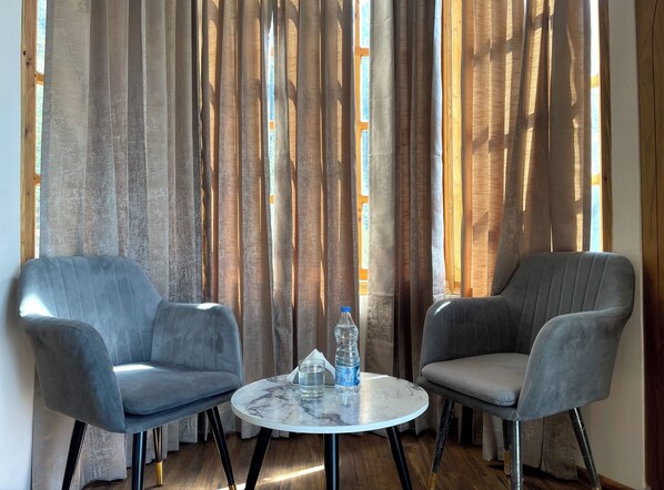A room with two grey armchairs and a small round table with a bottle of water and a glass. - Swastikam Homestay (Shimla)