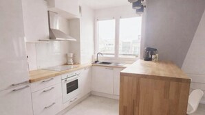A modern kitchen with white cabinets, a wooden countertop, a built-in oven, and a window with a city view. - Magic Stay Val d' Europe (Chessy)