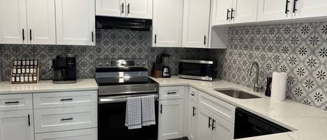 Una cocina moderna con armarios blancos, horno de acero inoxidable, cafetera y microondas.