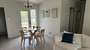 Un coin repas avec une table ronde et des chaises, un canapé blanc et des œuvres d’art accrochées aux murs.