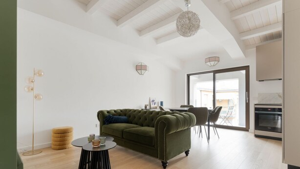 En moderne stue med en grøn sofa, et rundt sofabord og et spiseområde med stole.
