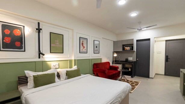 Un dormitorio con cama, una silla roja, escritorio y kitchenette.