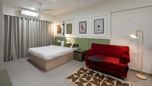Una habitación de hotel con una cama, un sofá rojo, una mesita, una lámpara de pie y un ventilador de techo.