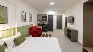 Una habitación de hotel con una cama, una silla roja, un escritorio, un televisor y un kitchenette.