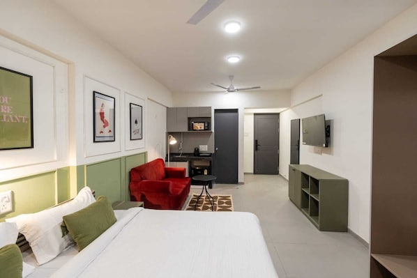 Una habitación de hotel con una cama, una silla roja, un escritorio, un televisor y un kitchenette.