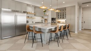 Une cuisine moderne dotée d’un îlot central, d’appareils électroménagers en acier inoxydable et de luminaires suspendus.