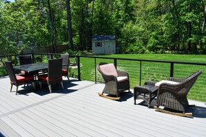 A deck with wicker furniture and a small shed in a wooded area. - Modern and Clean Four Bedroom House -nestled in conservation land! (Harwich)