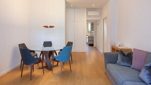 A modern living room with a glass dining table, blue chairs, a grey sofa with cushions, and a wooden floor. - easyhomes - Piazza Erculea (Milan)