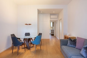 Ein modernes Wohnzimmer mit einem Glastisch, blauen Stühlen, einem grauen Sofa mit Kissen und einem Holzboden.