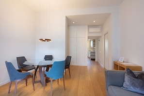 Ein modernes Wohnzimmer mit einem Glastisch, blauen und grauen Stühlen, einem grauen Sofa und Holzboden.