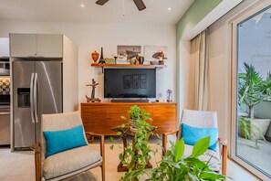 Un salon moderne doté d’un téléviseur à écran plat, de meubles en bois et d’une grande fenêtre donnant sur un paysage verdoyant.