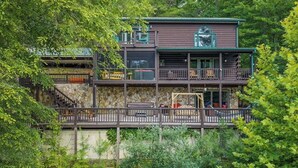 A multi-story cabin with a stone facade, wooden deck, and outdoor seating area. - RIVER, HOT TUB, GAME ROOM, PETS - 4 Pool, Playground, Dog Park, Arcade, Tennis. (Ellijay)